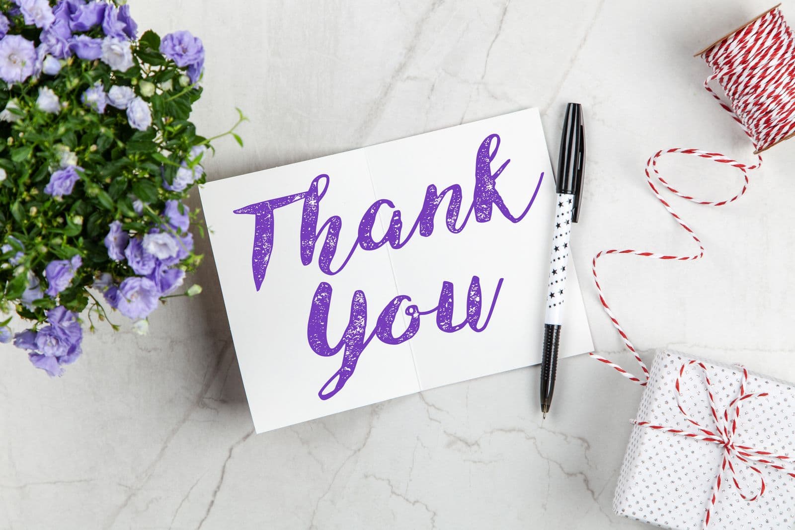 Thank you card, pen, and small gift on marble for a digital wedding thank you cards guide