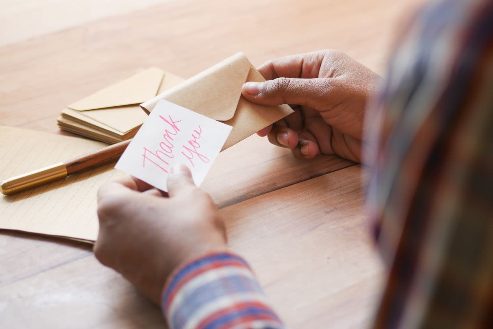 Hands holding a handwritten thank you card and envelope while planning digital wedding thank you cards