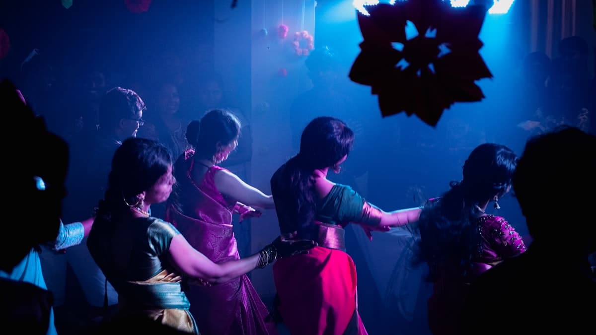 Women in traditional Indian attire dancing at a sangeet night celebration with colourful stage lighting