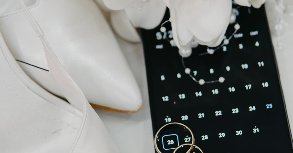 Wedding rings, flowers, and smartphone with calendar app for wedding RSVP management and guest planning